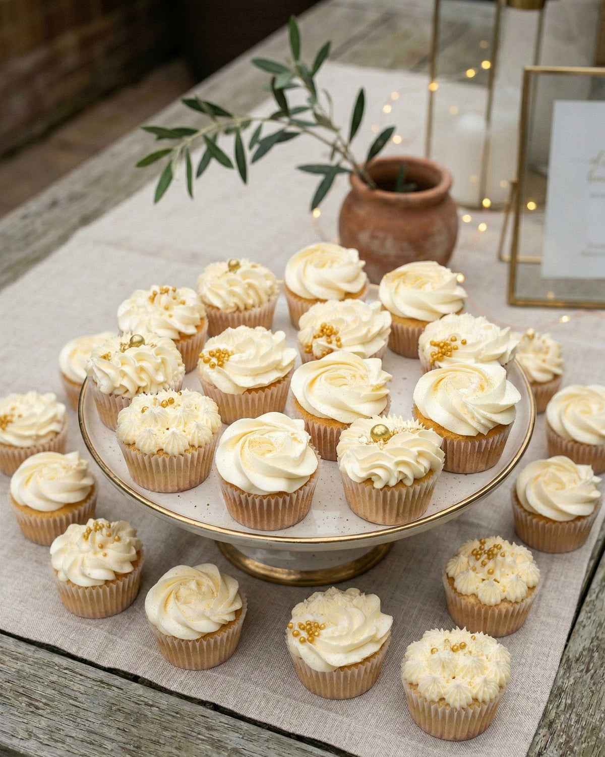 A tiered stand of vanilla cupcakes with swirled buttercream and gold sprinkles
