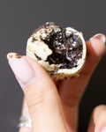 Oreo Protein Ball by La Sura Bakery, bitten to show the dark Oreo centre inside a white coating with cookie crumbs