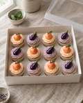 Peach and Aubergine Cupcakes: twelve cupcakes in white cases, rows of four, alternating soft peach buttercream swirls topped with a glossy sugar peach with a green leaf and lilac buttercream swirls topped with a glossy sugar aubergine with a green stalk, like the emoji
