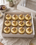 Pornstar Martini Cupcakes: twelve cupcakes in gold foil cases, rows of four, with pale yellow passion fruit buttercream swirls, each topped with half a fresh passion fruit, a drizzle of passion fruit seeds and a dusting of edible gold shimmer
