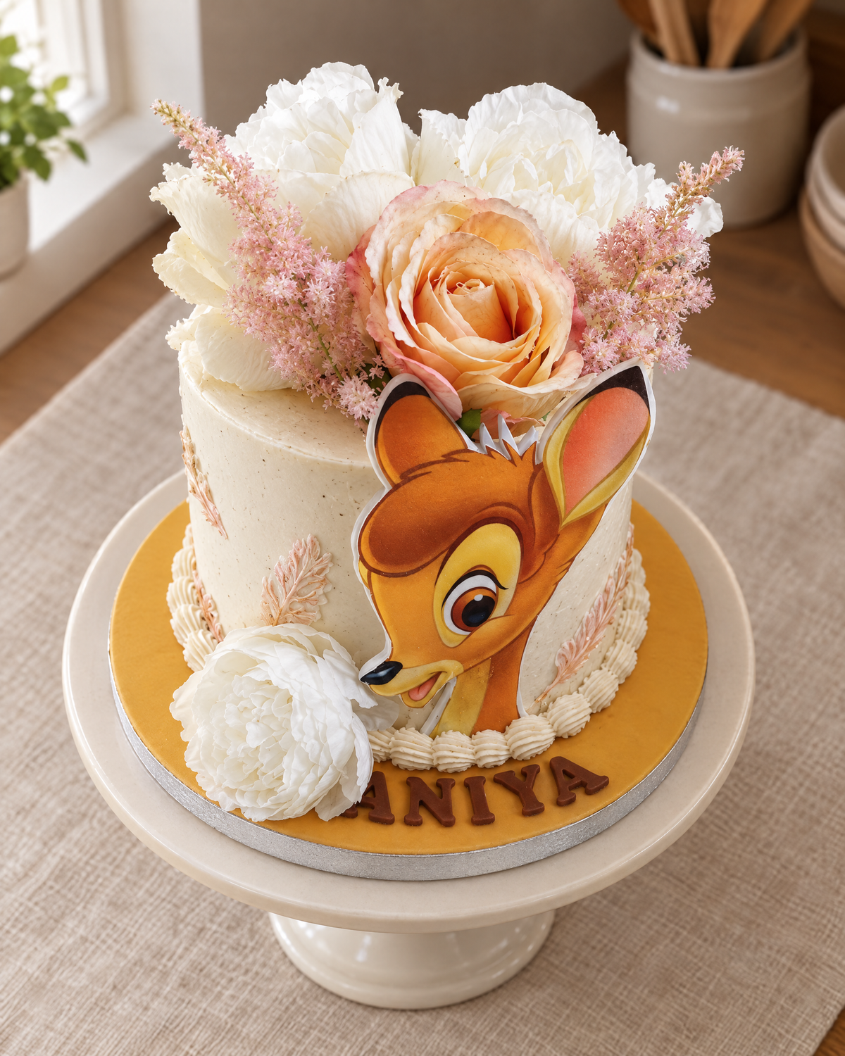Fawn Floral Cake: a tall white cake with a printed fawn topper, cream and peach roses, pink astilbe and a name in chocolate letters on a mustard board