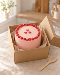 Small pink bento cake with a piped red heart border and three hearts, in a kraft bento box