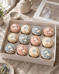 Hello World Baby Cupcakes: twelve cupcakes in white cases with soft blush pink, pale blue and cream swirls, topped with small white sugar clouds and four flat discs reading HELLO WORLD in grey