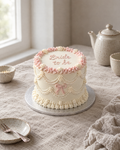 Bride to Be Lambeth Cake: smooth white buttercream with a blush pink ruffled top edge like a veil, strings of white sugar pearls looped between the swags, and a small piped blush bow on the front