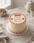 Dog Birthday Cake: a small round dog-safe cake, carrot and peanut sponge covered in smooth pale cream yoghurt frosting, a pink piped border, a dog bone-shaped biscuit and two small paw prints piped on the top