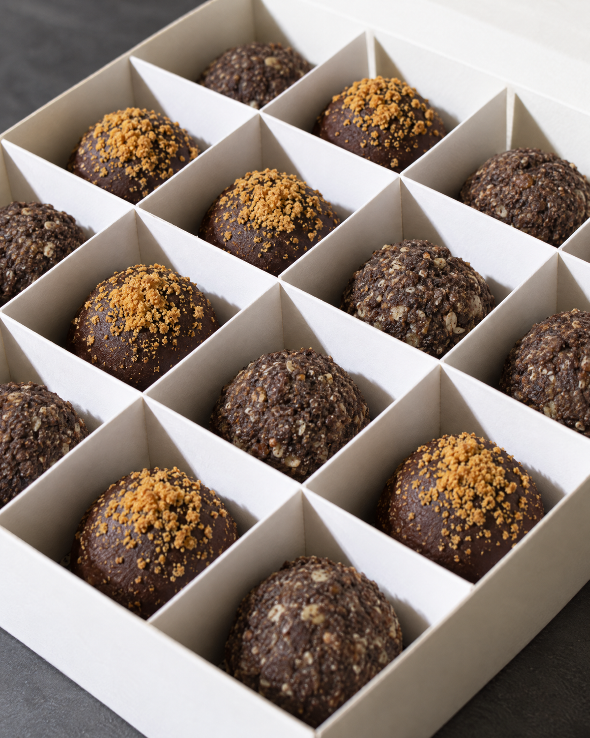 A box of Biscoff and Energy protein balls: chocolate balls topped with Biscoff crumb next to dark brown textured Energy balls