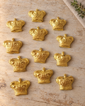 12 Gold Crown Cupcake Toppers laid flat on a wooden board